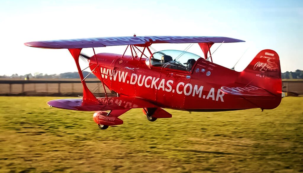 Impactante fotografía de biplano de color rojo del Grupo Duckas iniciando vuelo sobre el campo argentino. Portada Historia del Grupo Duckas.